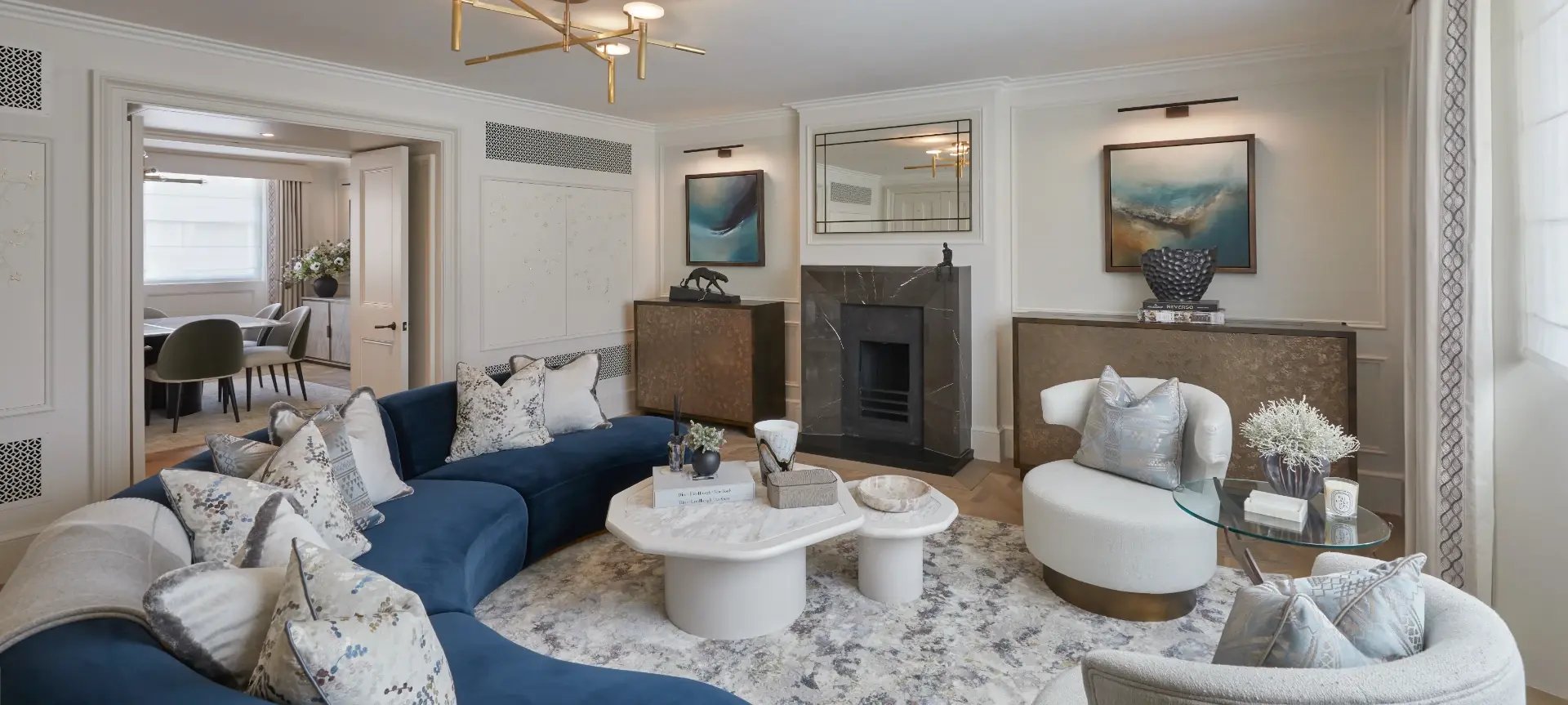 Elegant living room with a navy velvet sofa and cream armchairs dressed in bespoke patterned cushions, beside full-height patterned curtains